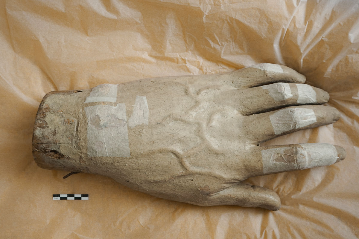 Anbringen von Japanpapier zur Sicherung von gelockerter Fassung an der Hand einer Skulptur vor dem Transport.